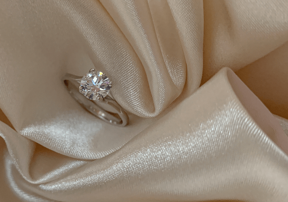 Solitaire diamond engagement ring on cream satin fabric, fine jewelry design